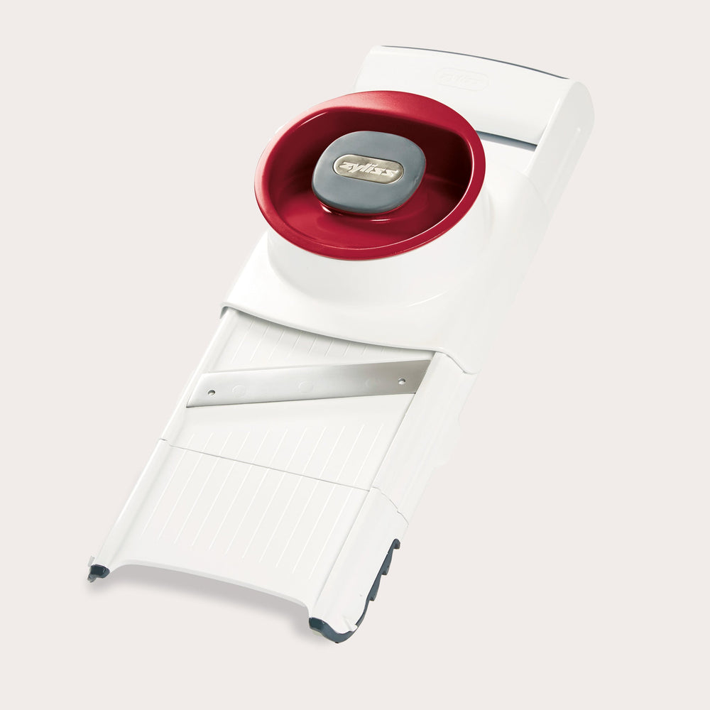 The Zyliss 4-in-1 Slicer & Grater in white and red, with a stainless steel blade and hand guard, sits on a light background—ideal for fast slicing or grating in any kitchen. 
