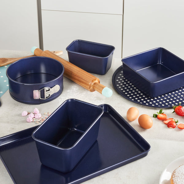 A kitchen counter displays Zyliss Durable Non-Stick Removable Base Cake Pans in blue, featuring a carbon steel body, along with a rolling pin, eggs, strawberries, and baking ingredients ready for use. #23cm/9"