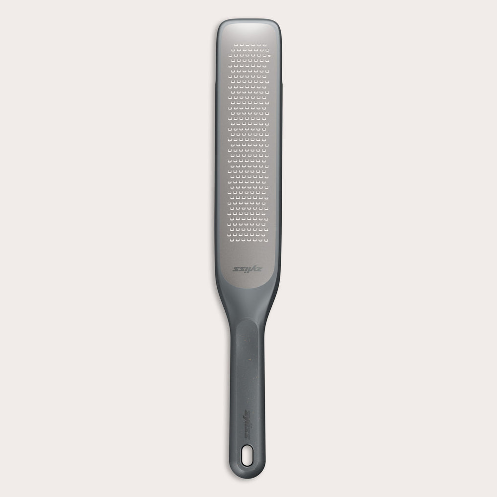 The Zyliss Rasp Grater is a long, rectangular foot file with a gray handle and textured metal surface for removing calluses and dead skin. The handle features a hanging hole for easy storage. 