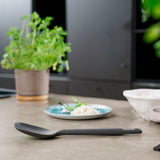 A Zyliss Spoon sits on a kitchen countertop, with a potted herb, a plate of white rice, and a white bowl softly blurred in the background. #Large