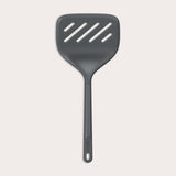 A Zyliss Turner XL slotted spatula in black, featuring a wide square head with three diagonal slots, ergonomic handle, and heat-resistant design is displayed against a plain light background. 