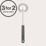 A Zyliss Gravy Whisk with a black handle is displayed upright on a light background. A 3 for 2 mix & match circular graphic appears in the top left corner. Ideal for preparing sauces.