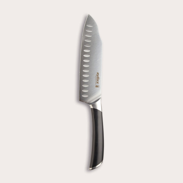 The Zyliss Comfort Pro Santoku Knife 18cm/7 features German stainless steel, a black ergonomic handle, and oval blade indentations, displayed against a light background. 